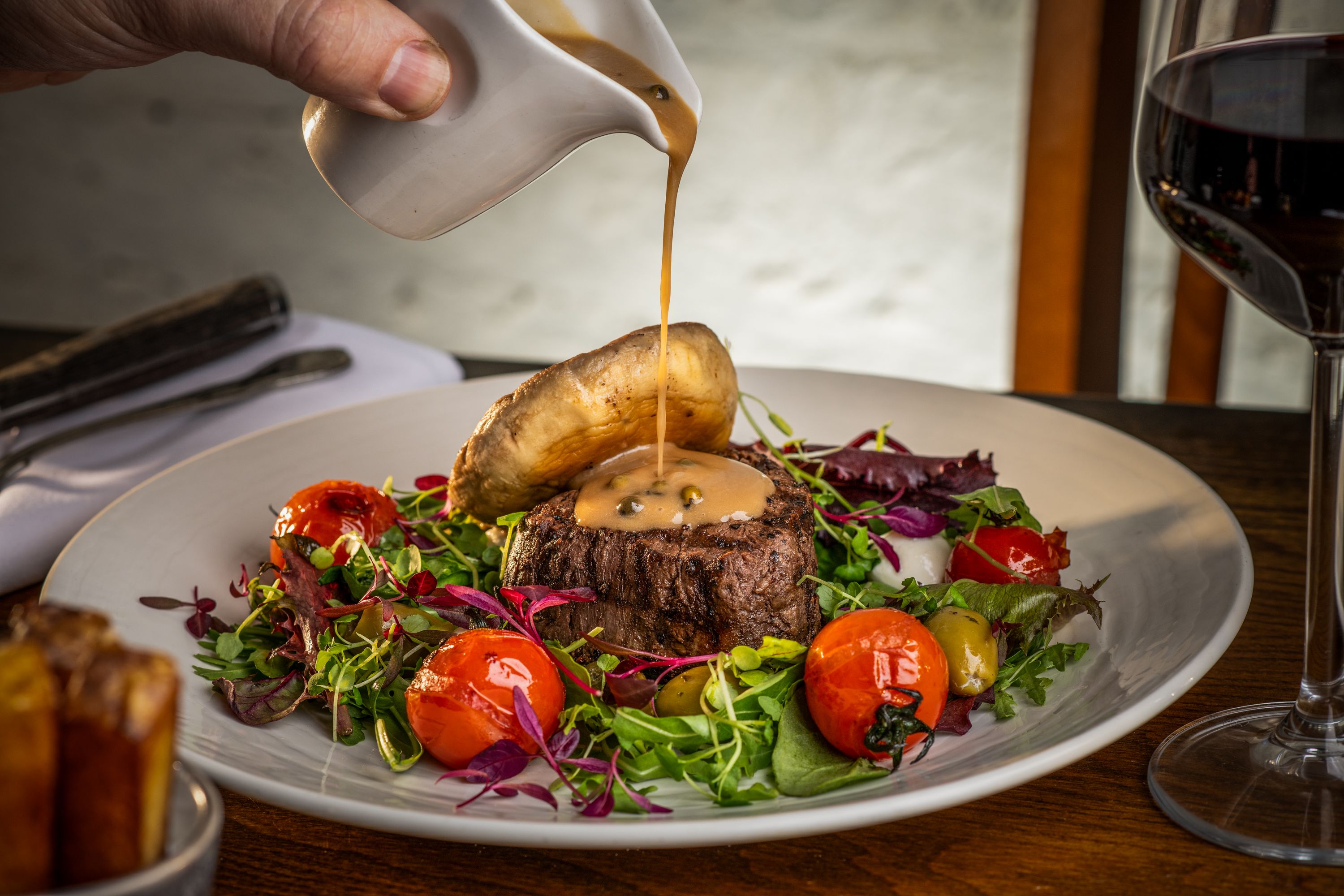 peppercorn sauce being poured over steak dish